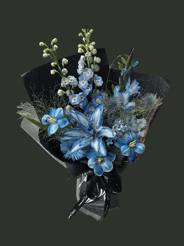 Full dyed blue lilies with blue delphinium, gerbera, eryngium, blue star flowers, silver mist foliage, and black wrapping