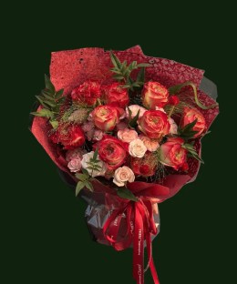 Coral-red and blush roses with greenery in layered red wrapping
