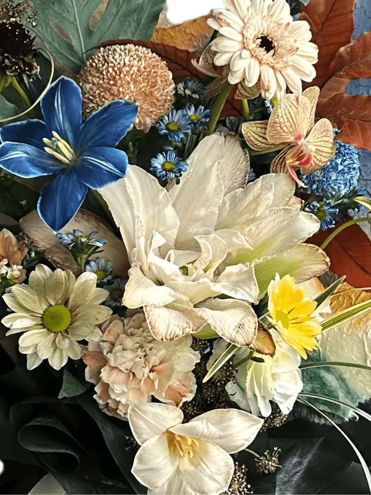 Close-up detail of double cream lilies with a dyed blue tulip, champagne gerbera and carnations, orchids, rust chrysanthemums, and autumn foliage