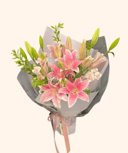 Full pink Oriental lilies, peach carnations, green lily buds, and fresh foliage in grey wrapping