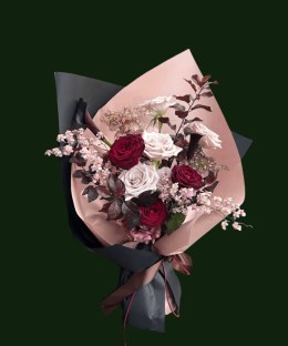 Blush and burgundy roses with airy accent flowers in layered pink and black wrapping.