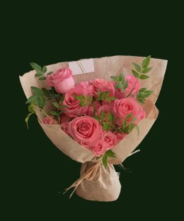 Bright pink roses in a fresh hand-tied bouquet with greenery and natural paper wrapping.