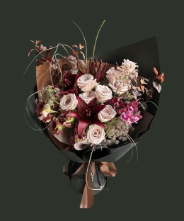 Full burgundy lilies and phalaenopsis orchids with grey-blush Manta roses, wine lisianthus, dark foliage, and curling grass