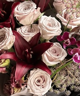 Close-up detail of burgundy lilies and phalaenopsis orchids with grey-blush Manta roses, wine lisianthus, dark foliage, and curling grass