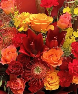 Close-up of red lilies, red roses, and orange pincushion protea in the Crimson Celebration Grande Bouquet