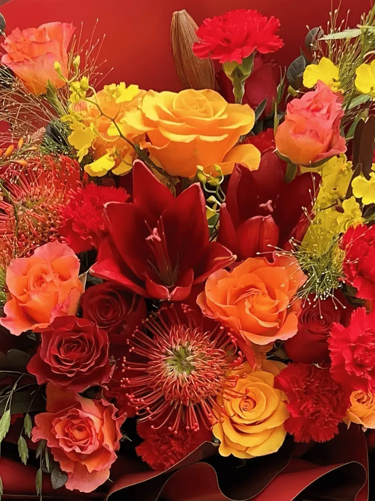 Close-up of red lilies, red roses, and orange pincushion protea in the Crimson Celebration Grande Bouquet