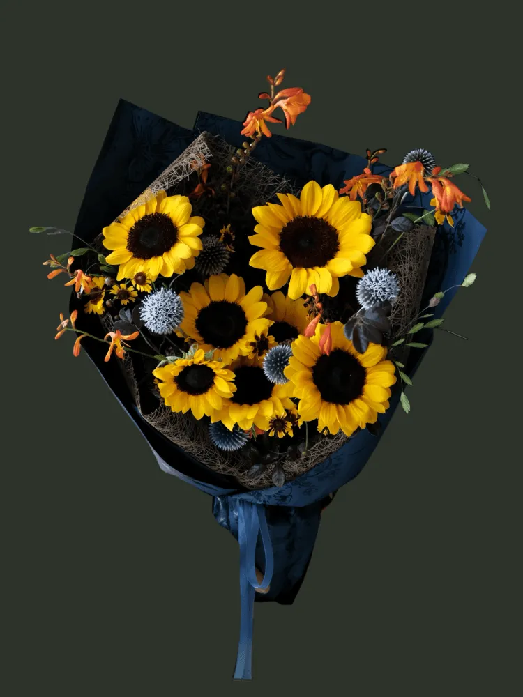 Full dark-centred yellow sunflowers with steel-blue eryngium, orange crocosmia, small daisies, and dark foliage in navy wrapping