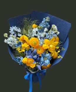 Full yellow ranunculus, tulips, cymbidium orchids and poppies with blue iris, delphinium, hydrangea, and stock