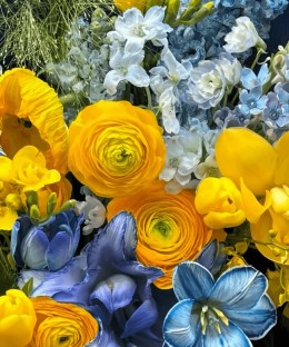 Close-up detail of yellow ranunculus, tulips, cymbidium orchids and poppies with blue iris, delphinium, hydrangea, and stock
