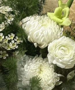Close-up of white chrysanthemums and ranunculus with green gladiolus, waxflower, and fern