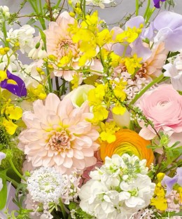 Close-up detail of blush dahlia, purple iris, pink and orange ranunculus, sweet pea, oncidium, and airy flowering branches