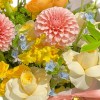 Close-up detail of pink pompon dahlias, cream roses, orange ranunculus, yellow calla lily, oncidium, and blue tweedia