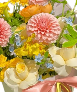 Close-up detail of pink pompon dahlias, cream roses, orange ranunculus, yellow calla lily, oncidium, and blue tweedia