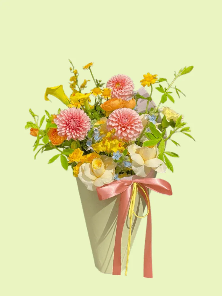 Full pink pompon dahlias, cream roses, orange ranunculus, yellow calla lily, oncidium, and blue tweedia