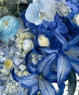 Close-up of dyed cobalt lilies, blue hydrangea, marbled roses, pale orchids, chrysanthemums, eryngium, and yellow craspedia in porcelain