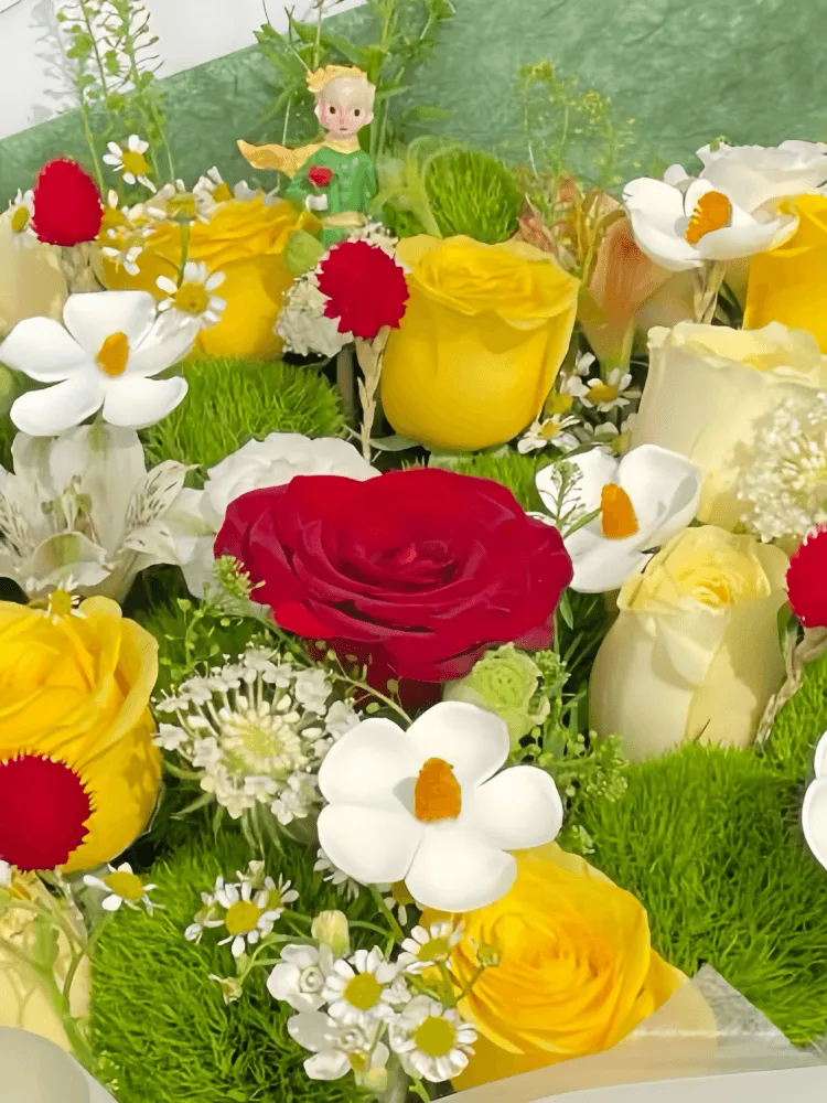 Close-up detail of red yellow and cream roses, Green Trick dianthus, white ranunculus, meadow flowers, and a Little Prince figure