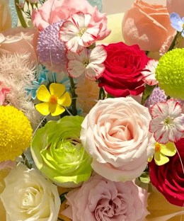 Close-up of pink gerbera, red and cream roses, green ranunculus, button mums, dianthus, and blue accents