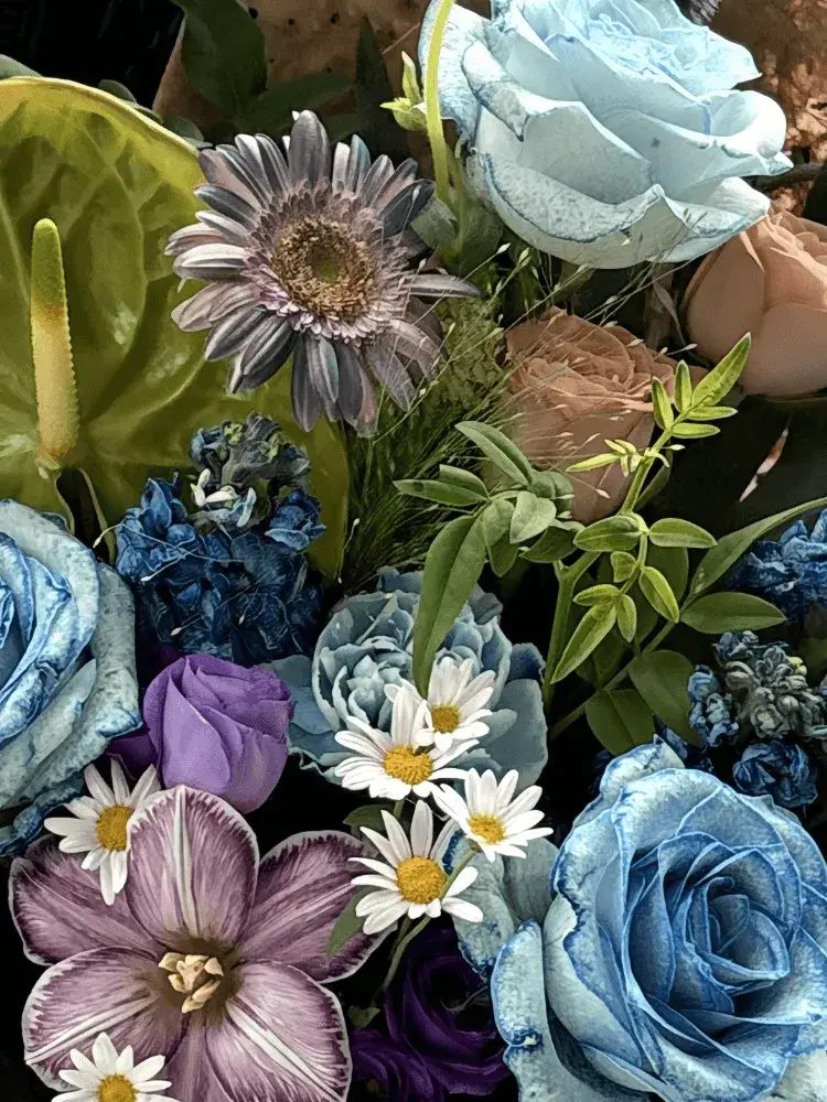 Close-up detail of dyed blue roses with green anthurium, mauve gerbera, striped tulip, blue delphinium, thistles, daisies, and red gomphrena