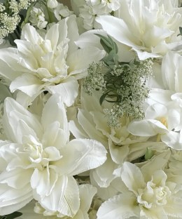 Close-up of double white lilies, white gladiolus, ivory line flowers, lace flower, and fresh green foliage