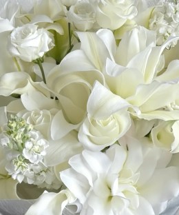 Close-up of white Oriental lilies, white roses, ivory stock, and green foliage in cool grey wrapping