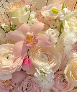 Close-up of blush ranunculus, pink orchids, cream roses, white line flowers, gerbera, tulip, and feathers