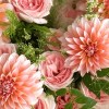 Close-up of peach dahlias, blush roses, green filler, white lace flower, fountain grass, and ivory wrapping
