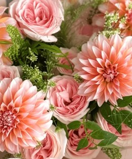Close-up of peach dahlias, blush roses, green filler, white lace flower, fountain grass, and ivory wrapping