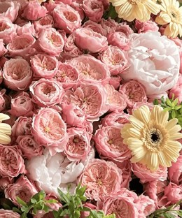 Close-up of peach spray roses, cream peonies, pale-yellow gerbera, green foliage, and natural brown wrapping