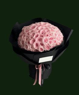 Pale pink garden-style roses arranged in a rounded black-wrapped bouquet with a pink ribbon.