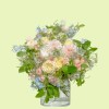 Full cream garden roses, pink dahlias and peony, blue delphinium, and airy white flowers in a clear vase