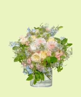 Full cream garden roses, pink dahlias and peony, blue delphinium, and airy white flowers in a clear vase