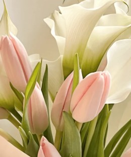 Close-up of blush-pink tulips, white calla lilies, natural green leaves, and pale mint wrapping
