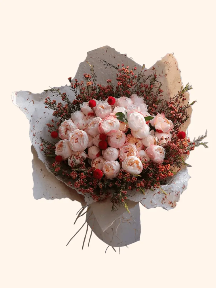 Full blush peonies, red globe flowers, coral waxflower, dark foliage, and cream wrapping