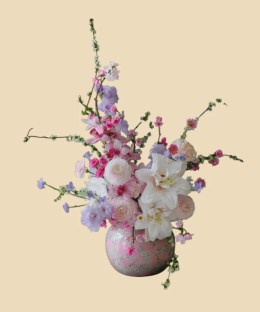 Full white double lilies, blush ranunculus, cymbidium orchids, flowering branches, gladiolus, and pale delphinium in pink porcelain