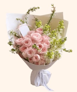 Full peach-pink garden roses, ivory-green stock, flowering spiraea, fresh foliage, and white wrapping