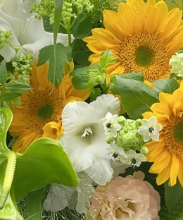 Close-up detail of sunflowers, green anthurium, white gladiolus, and soft seasonal flowers in a green-and-yellow bouquet