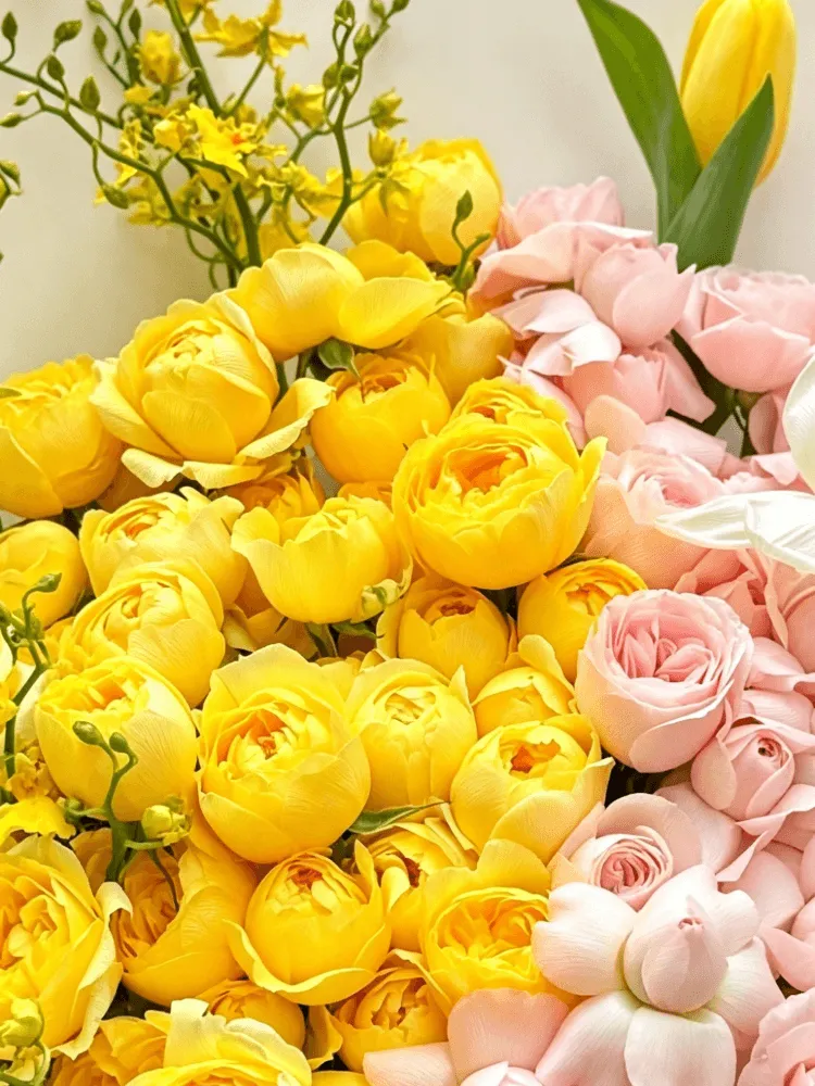 Close-up of yellow garden roses, blush spray roses, yellow oncidium, yellow tulip, and white bulb flowers