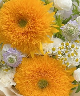 Close-up detail of two Teddy Bear sunflowers with white lisianthus, campanula, chamomile, purple scabiosa, and eucalyptus