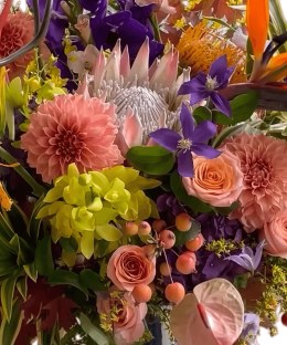 Close-up of blush protea, bird of paradise, peach dahlias, orchids, anthurium, roses, berries, and autumn foliage